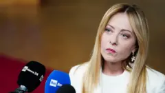 Giorgia Meloni, primera ministra de Italia, vestida de blanco frente a dos micrófonos