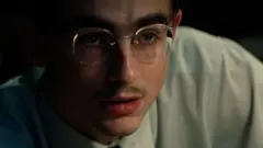 Close de Timothée Chalamet de óculos, bigode e camiseta no filme 'Marty Supreme'