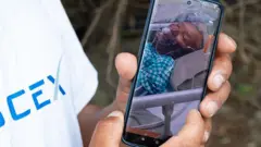 Una persona sostiene un teléfono donde se ve la foto del guía Dawa Sherpa con una máscara de oxígeno acostado en una cama.