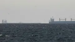 A cargo ship is seen on the horizon in the Gulf, near the Strait of Hormuz