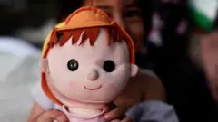 Una de las hijas de Milagros González jugando con una muñeca. Se ve una muñeca de tela sonriendo.