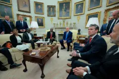 Várias pessoas em salão, com Trump e Ramaphosa sentados ao fundo