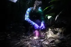 Uma mulher com uma lanterna presa na cabeça enquanto coloca camisinha em uma torre de argila