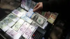 نمایی از ریال و دلار ایران پس از نرخ دلار که افزایش آن در روزهای اخیر مهار نشد، در تاریخ ۲۶ آذر ۱۴۰۳با عبور از ۷۷ هزار تومان در تهران، رکورد تاریخی خود را شکست