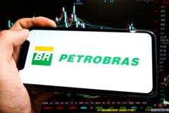 Logo da Petrobras no celular; atrás, está uma tela com gráficos