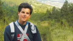 Acutis de moletom e mochila, numa paisagem montanhosa