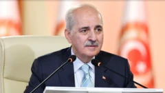Numan Kurtulmuş beyaz bir deri koltukta oturuyor, arkada türk bayrağı var. 