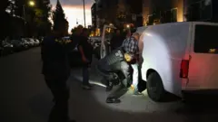 Agentes do Serviço de Imigração e Controle de Alfândegas dos Estados Unidos (ICE, na sigla em inglês) revistam um homem ao lado de uma van branca