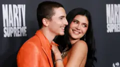 Timothée Chalamet, em um terno laranja, e Kylie Jenner, em um vestido laranja combinando, aparecem juntos e sorrindo na estreia