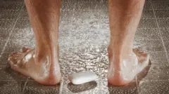 Sabonete no chão do box entre as pernas de um homem