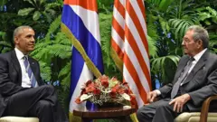 Os ex-presidentes dos Estados Unidos, Barack Obama, e de Cuba, Raúl Castro, sentados em frente às bandeiras dos dois países