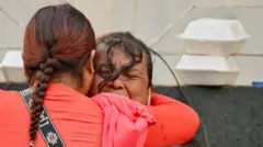 Una mujer con una camiseta manga larga roja abraza a otra mujer, que llora desconsolada. 