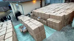 Desetine kutija ispred kuće i nekoliko ljudi čija su lica zamagljena