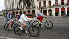 Três turistas passeiam de bicicleta em Havana