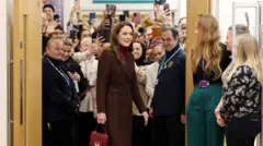 Kate Middleton, uma mulher branca e alta, de cabelos castanhos compridos