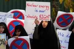 Um estudante iraniano segura uma placa com os dizeres "A energia nuclear é nosso direito absoluto" durante uma manifestação em frente ao reator de pesquisa de Teerã em 23 de novembro de 2014, para mostrar apoio ao programa nuclear do Irã.