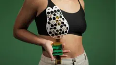 A woman showing the ultrasound device placed over a bra cup