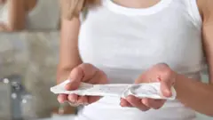 Женщина держит в руках свежую прокладку, ее лица не видно, только руки и верхняя часть тела в белой майке.