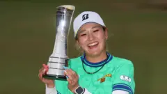 ミントグリーンのシャツを着た桑木が両手でトロフィーを顔の横に持ち上げて笑顔を見せている
