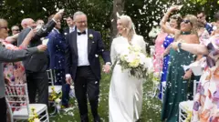 Australian Prime Minister Anthony Albanese and Jodie Haydon walk down the aisle towards the camera. Guests throw confetti over the couple
