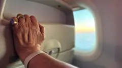 Mão agarrando o assento de um avião. Ao fundo, pode-se ver o horizonte pela janela.