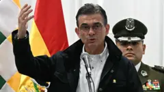 El presidente Rodrigo Paz, que lleva lentes, una camisa blanca y una chaqueta negra, habla frente a un micrófono.