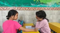 Dos niñas se sientan una frente a la otra en un aula escolar en la ciudad de Bombay.