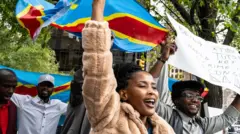 Les manifestants sourient en brandissant des drapeaux congolais et des pancartes, dont l'une porte la mention « Être Tutsi ne devrait pas être un crime au Congo ».