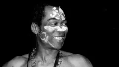 Fela Kuti, no wear shirt wit white paint for im face and big chain around im neck, dey perform for stage for Detroit, Michigan, for 1986.
