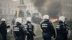 Protestos em frente às instituições europeias, em Bruxelas (Bélgica). Vários policiais cercam um trator e uma pequena queimada