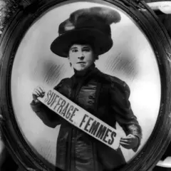 Retrato de Hubertine Auclert, uma das pioneiras do movimento sufragista na França, com uma faixa nas mãos com os dizeres 'suffrage femmes'