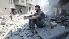 Homem sentado sobre escombros na Faixa de Gaza