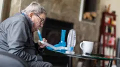 Pessoa idosa sentada sopra no tubo de um aparelho para medir sua capacidade pulmonar