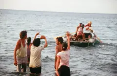 Cubanos deixam a costa em pequenas embarcações enquanto outros, com as pernas dentro da água, acenam em despedida