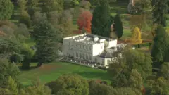 Royal Lodge dilihat dari atas pada 21 Oktober 2025. Bangunan ini berupa bangunan persegi panjang besar berwarna putih dengan atrium di bagian bawahnya, terletak di lahan yang rimbun. Beberapa pohon memiliki daun berwarna cokelat sementara yang lain berwarna hijau seiring pergantian musim dari musim panas ke musim gugur.