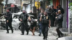 Policiais escoltam um suspeito preso durante a Operação Contenção na favela da Vila Cruzeiro, no complexo da Penha, no Rio de Janeiro, Brasil, em 28 de outubro de 2025