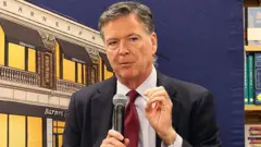 Tek elini kaldırmış bir adam diğer elinde mikrofonla konuşuyor