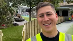 Dallan Tan, de colete, sorrindo em frente a um novo parquinho