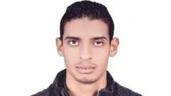 アル・シャズリー死刑囚の首から上の写真。口の上下にひげが生えている。正面を見ている。背景は白