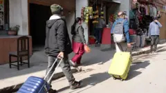 सुटकेश डोर्याएर तानीरहेका दुई जना श्रमिकहरूको तस्बीर