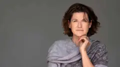 Uma mulher olhando para a câmera, com a mão esquerda apoiada no queixo