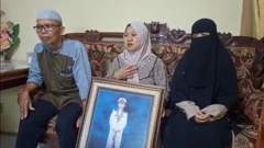 La familia del capitán Ashari Samadikun en Indonesia sentada en un sofá durante una entrevista. La mujer en el centro sostiene un retrato grande de él enmarcado.