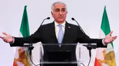 Reza Pahlevi está falando em um púlpito e com os braços abertos