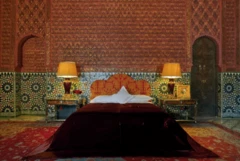 Fotografía interior de una de las habitaciones, con una cama en el centro, paredes llenas de azulejos, mesitas de noche con lámparas suntuosas y cama ricamente decorada.
