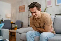 Homem sentado em sofá se contorcendo de dor