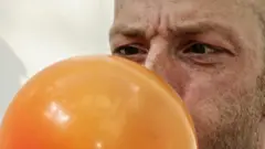 Homem soprando um balão de gás de cor laranja