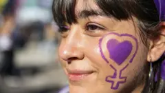 A woman with a purple heart and woman symbol painted on her face