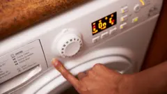 A hand is shown pressing a button on a washing machine