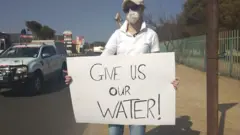 ውሃችንን ስጡን የሚል ፖስተር የያዘች ሴት