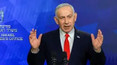 O primeiro-ministro israelense Benjamin Netanyahu usa terno preto e gravata vermelha, em pé contra um fundo azul com o logotipo oficial do Gabinete do Primeiro Ministro
